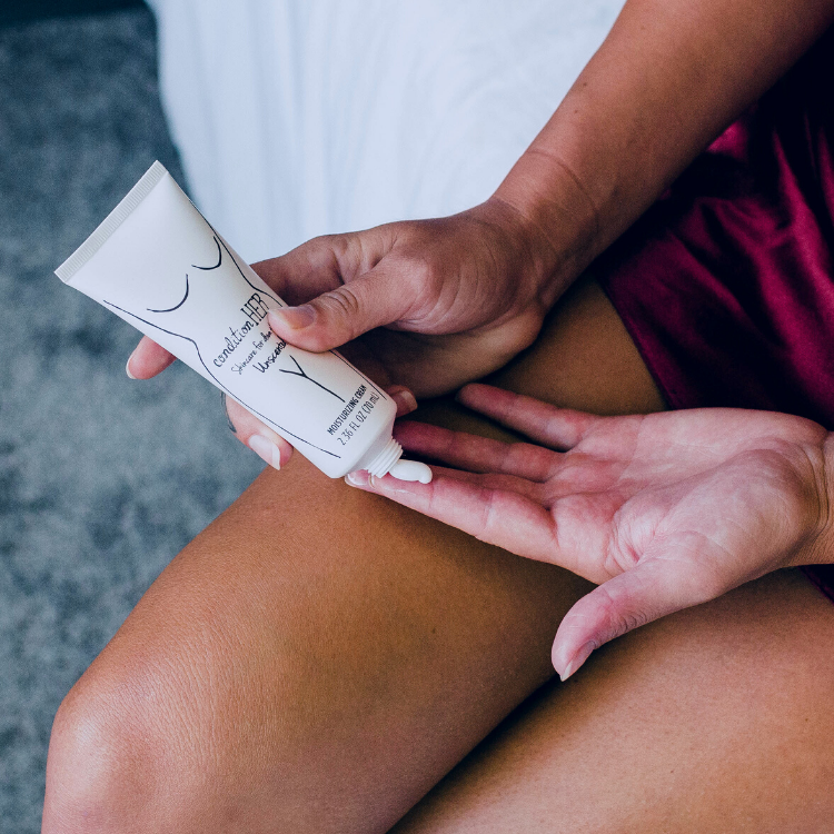 Woman applying conditionHER cream in red silk slip on bed edge